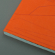 Livre à couverture rigide orange avec une illustration au trait minimal repose sur une surface grise, présentant un design graphique exquis.