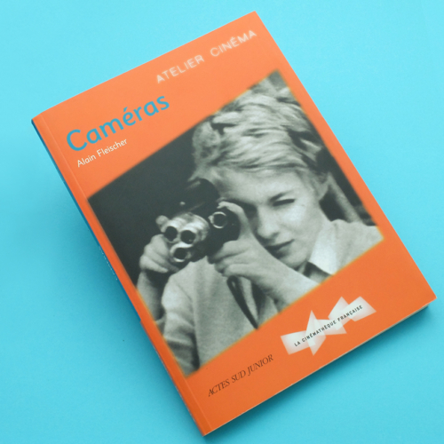 Un livre orange intitulé « Appareils photo » présente une illustration saisissante en noir et blanc d'une personne utilisant un appareil photo vintage sur la couverture, sur fond bleu vif.