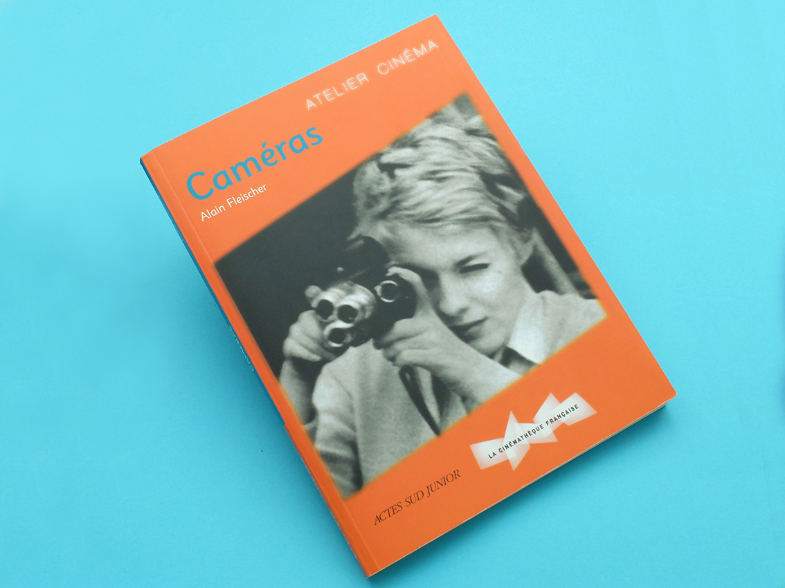 Un livre orange intitulé « Appareils photo » présente une illustration saisissante en noir et blanc d'une personne utilisant un appareil photo vintage sur la couverture, sur fond bleu vif.