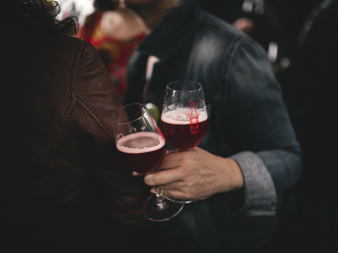 Une illustration montre deux individus portant des vestes décontractées, trinquant avec des verres de vin naturel dans un cadre social animé.