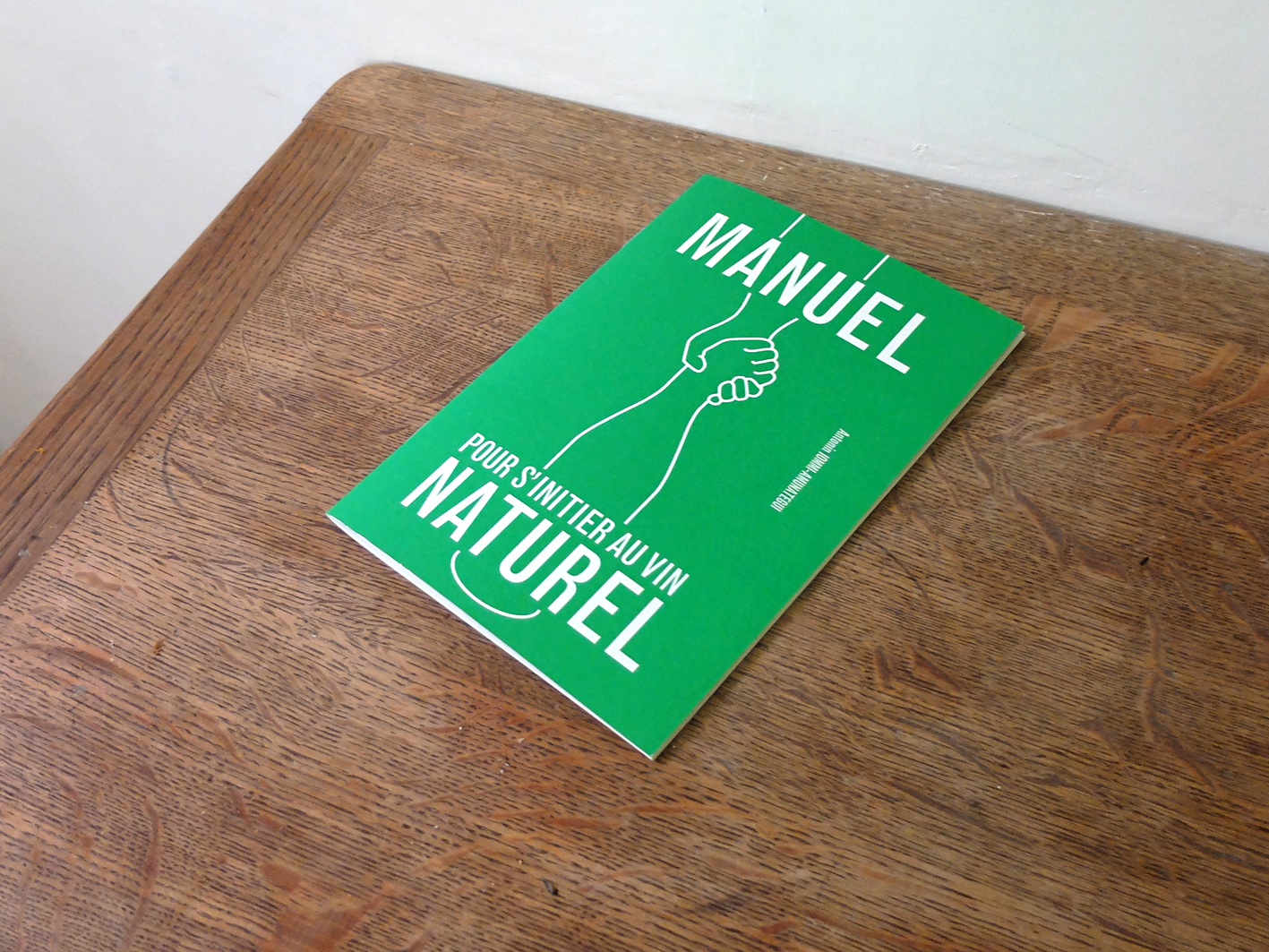 Livret vert intitulé "Manuel Pour S'Initier au Vin Naturel" avec une illustration de bon goût sur la couverture, reposant sur une surface en bois.