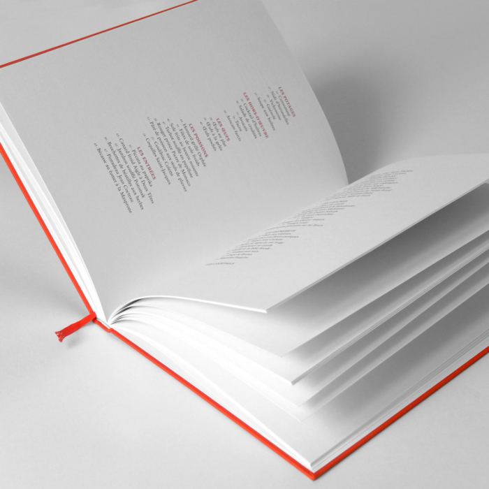 Livre ouvert avec une couverture rouge et un marque-page en ruban, affichant des pages remplies de texte. Le livre est placé sur une surface blanche.