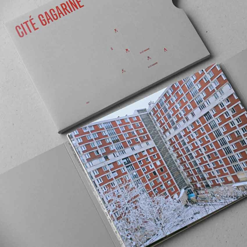 Un livre ouvert révèle une photo d'un immeuble de grande hauteur rouge et blanc, à côté d'une enveloppe partiellement visible étiquetée « Cité Gagarine ».