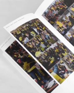 Gros plan sur un livre ouvert dont les pages sont remplies de photos de personnes vêtues de gilets jaunes, rassemblées dans des lieux clos bondés.